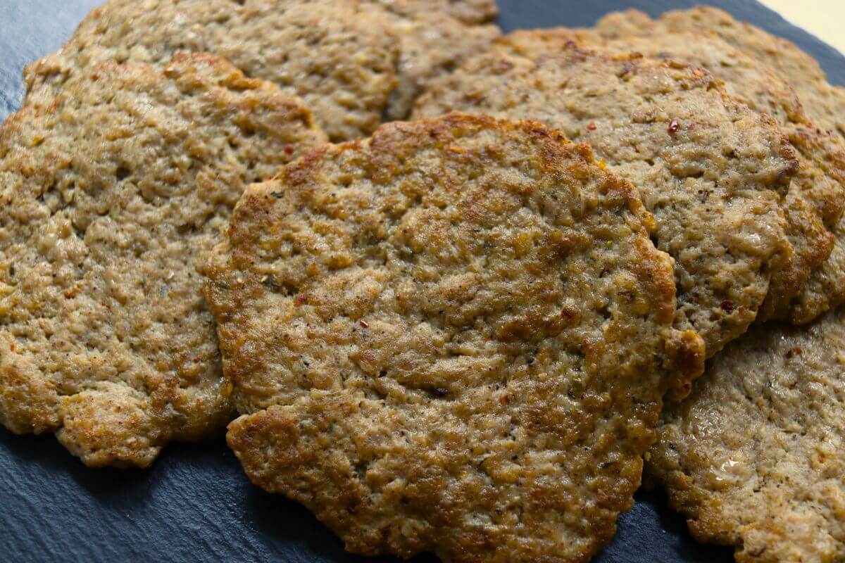Thin homemade breakfast sausage patties with browned surfaces arranged together on a dark serving surface.