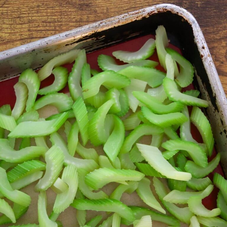Sliced celery spread in a single layer on a baking sheet before freezing.