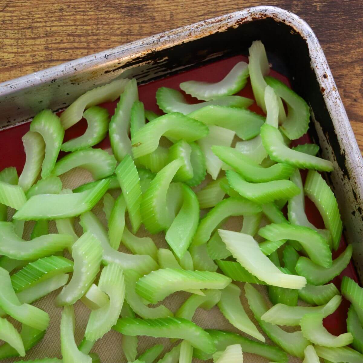 Sliced celery spread in a single layer on a baking sheet before freezing.