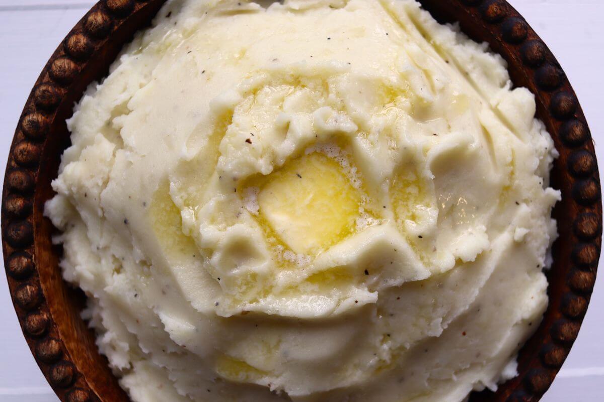 Fluffy homemade mashed potatoes served in a wooden bowl with a pool of melted butter.