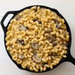 Creamy mushroom macaroni and cheese with cavatappi pasta in a black cast iron skillet.