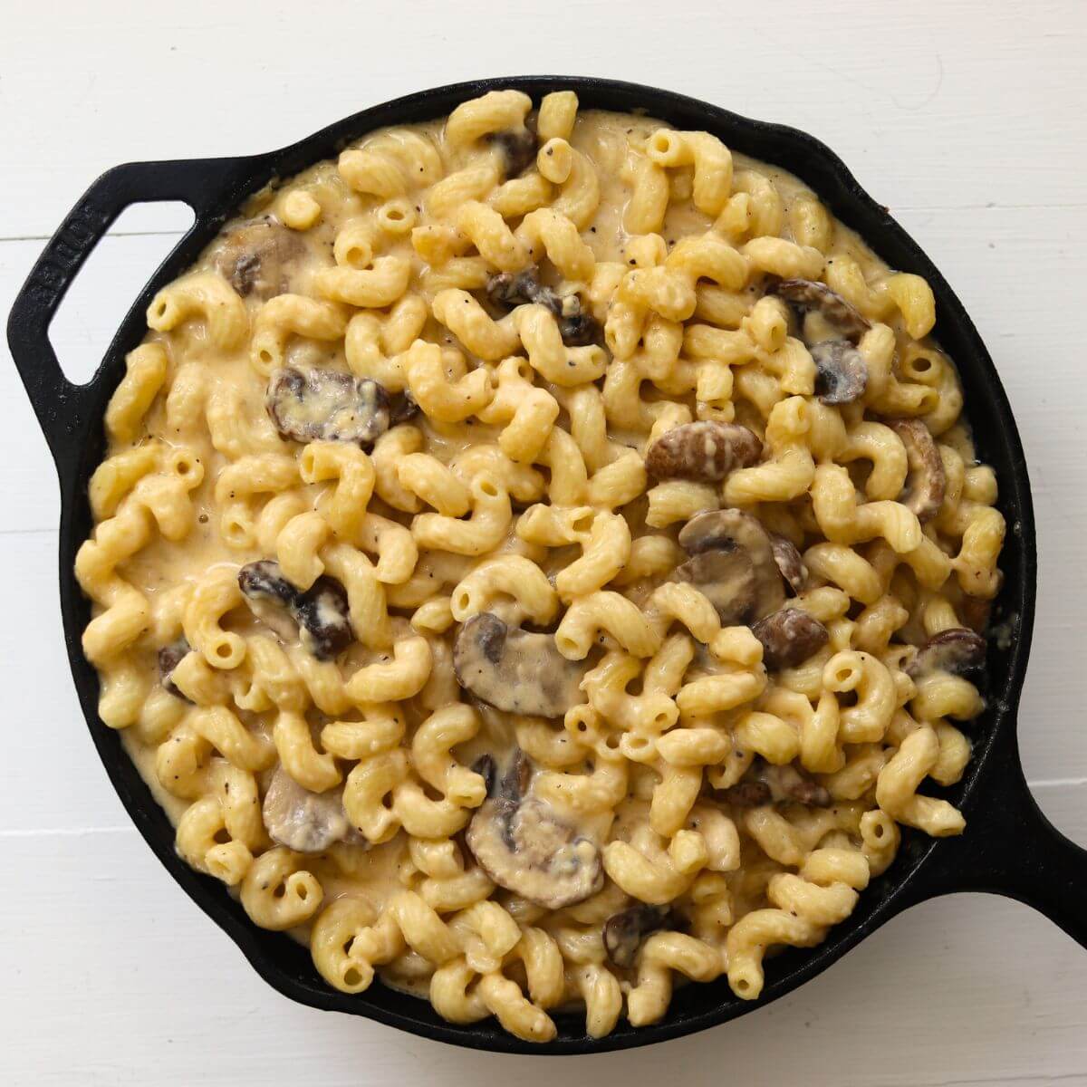 Creamy mushroom macaroni and cheese with cavatappi pasta in a black cast iron skillet.