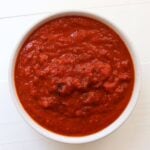 Thick pizza sauce from scratch with visible tomato pieces and herbs in a white bowl.