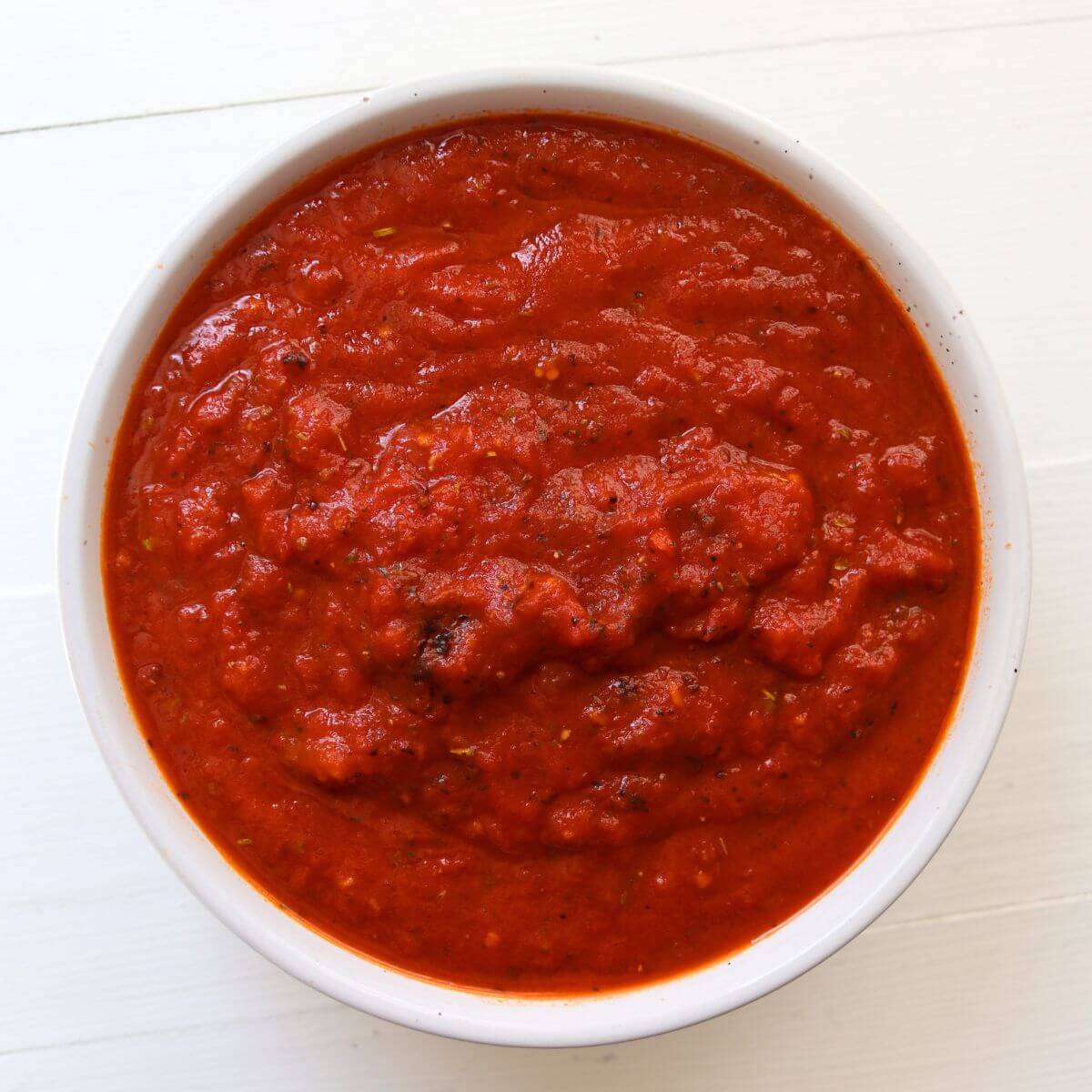 Thick pizza sauce from scratch with visible tomato pieces and herbs in a white bowl.