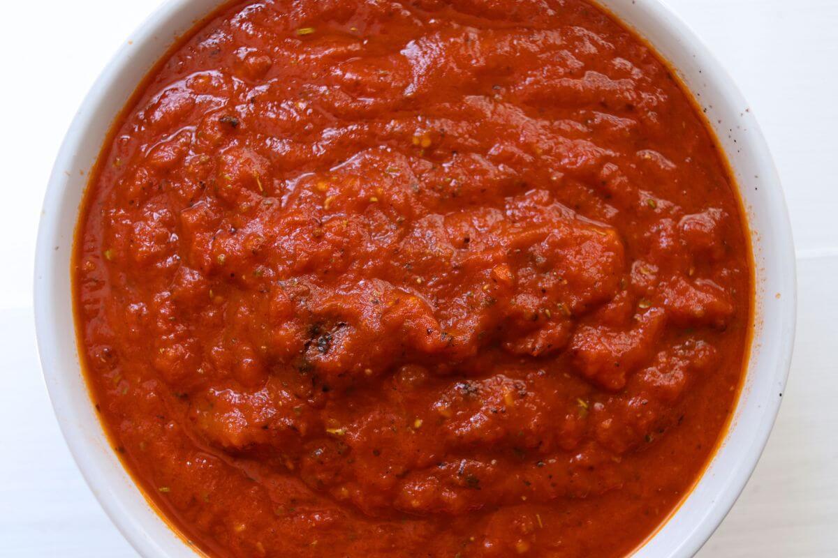 Red homemade pizza sauce with a thick, textured consistency and visible Italian herbs.