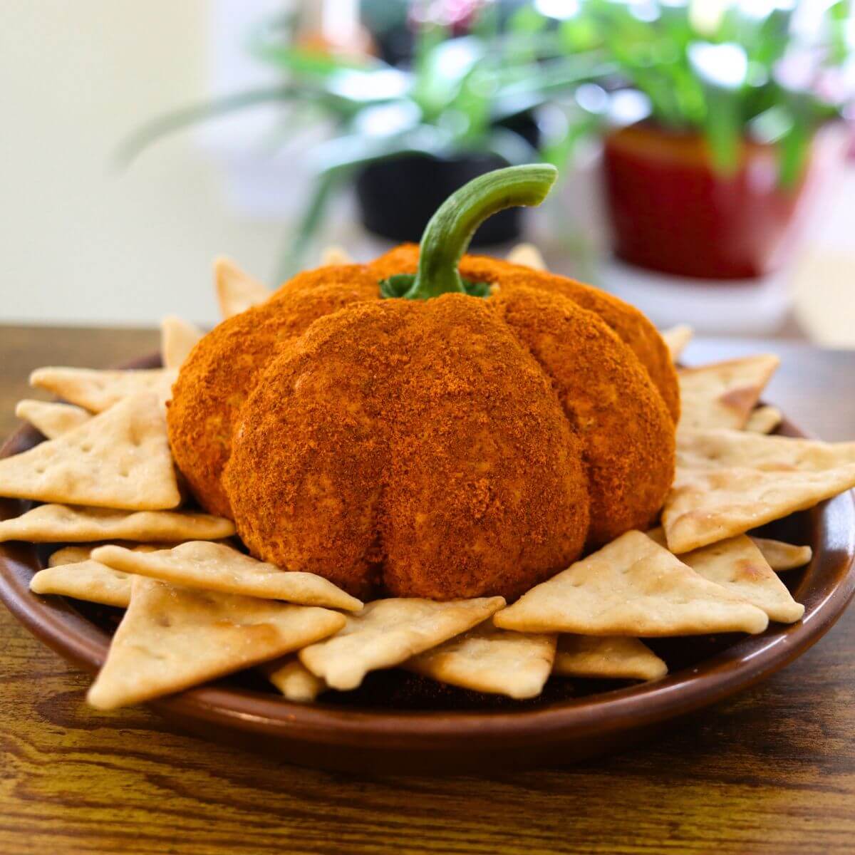 Pumpkin cheese ball shaped like a pumpkin with a green stem and crackers on a serving plate.