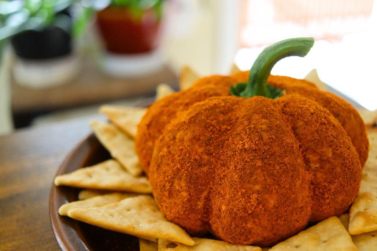 Savory pumpkin-shaped cheese ball coated in orange seasoning and served with crisp crackers for a fall appetizer.