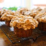 Pumpkin crumb muffin with cinnamon streusel topping and vanilla icing on a cooling rack.