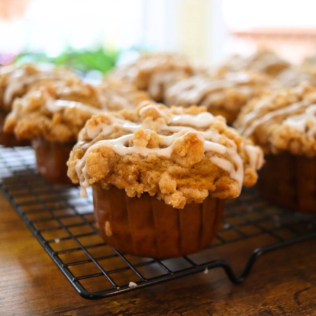 Pumpkin crumb muffin with cinnamon streusel topping and vanilla icing on a cooling rack.