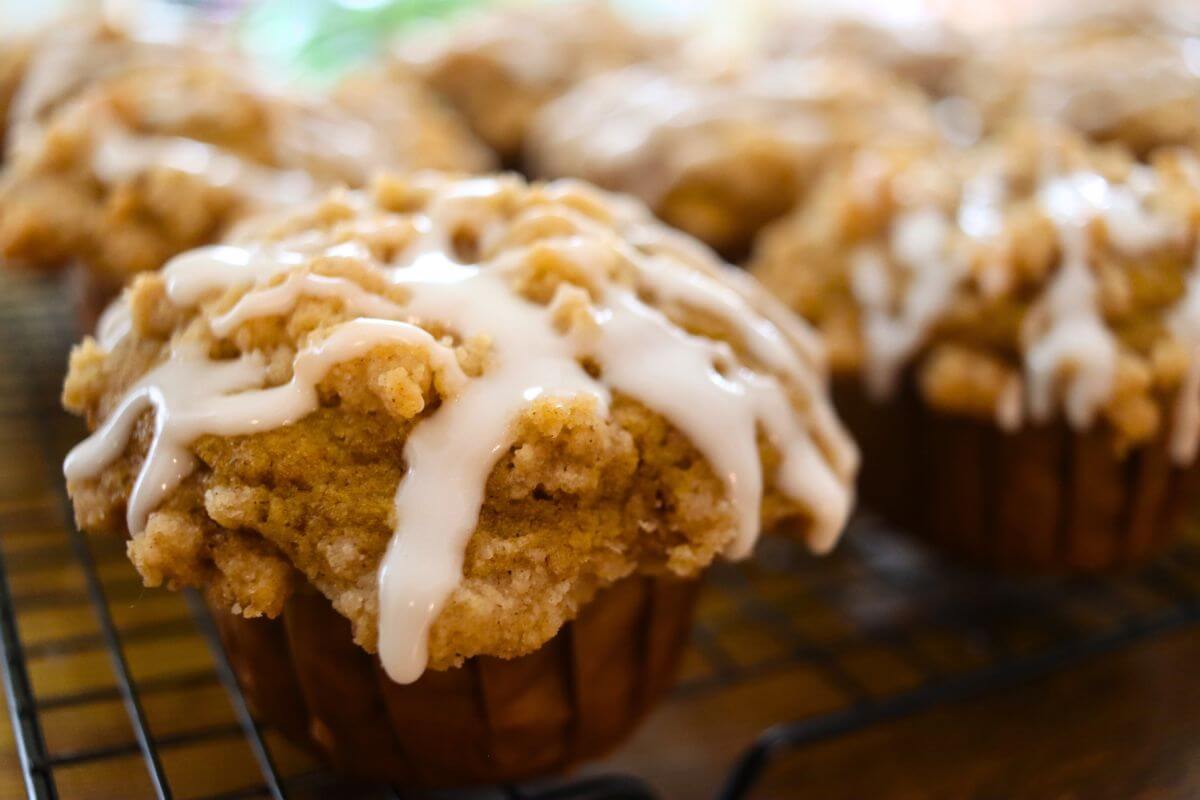 Iced pumpkin crumb muffins with buttery streusel topping cooling on a wire rack.
