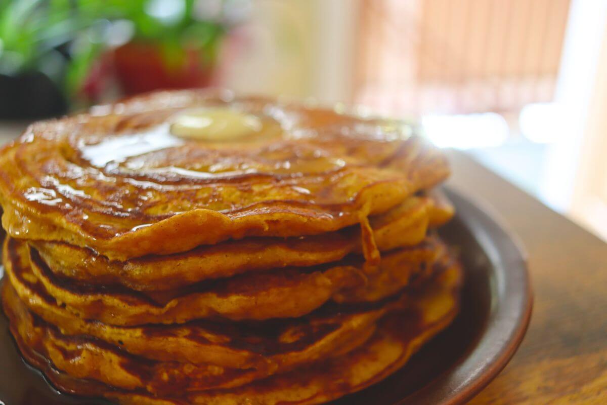 Homemade pumpkin spice pancakes stacked high with melting butter and maple syrup.