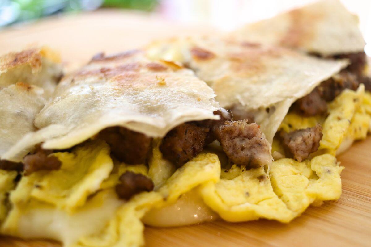 Golden tortilla quesadilla with scrambled eggs, crumbled breakfast sausage, and melted cheese filling.