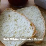 Homemade soft white sandwich bread with a soft, airy crumb, raspberry jam, and a butter crock. Text overlay: "Soft White Sandwich Bread".