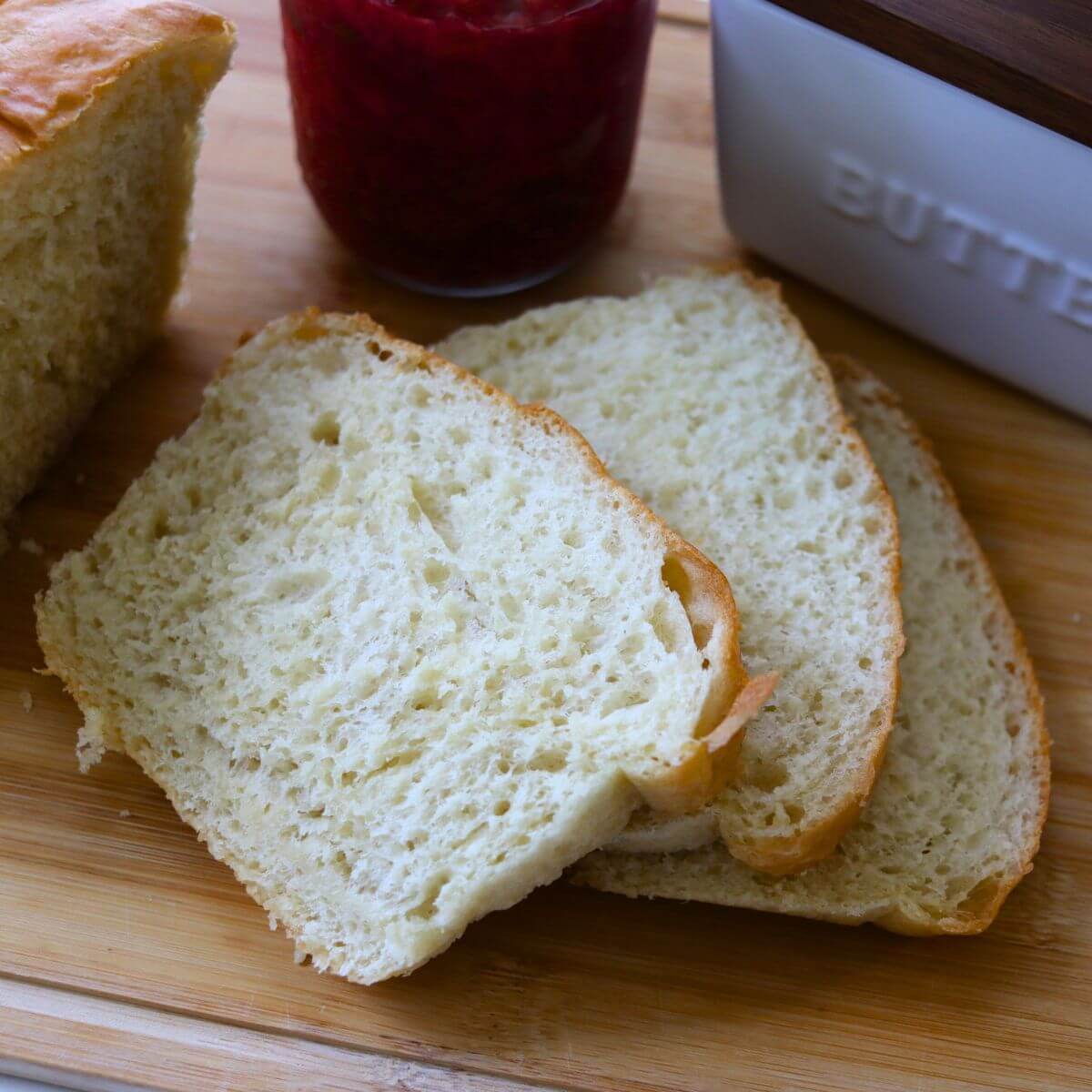 Homemade soft white sandwich bread with sliced loaf, raspberry jam, and a butter crock.