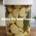 Jar of spicy pickled garlic with red pepper flakes and bay leaf, labeled “Spicy Pickled Garlic".