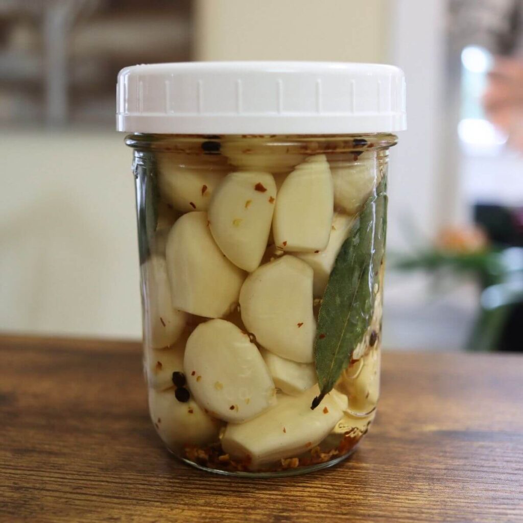 Jar of spicy pickled garlic cloves with red pepper flakes, peppercorns, and bay leaves.