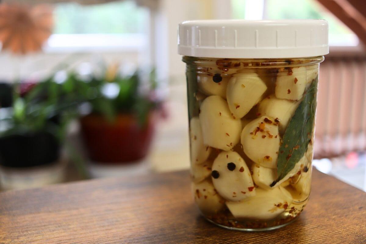 Jar of spicy pickled garlic cloves with red pepper flakes, peppercorns, and bay leaves.