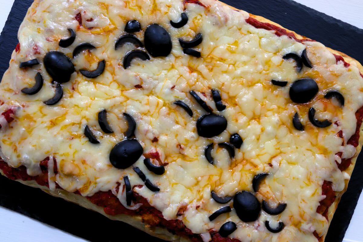 Rectangular cheese spider pizza topped with black olive bodies and curved olive legs.