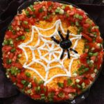 Halloween spider web dip surrounded by blue corn tortilla chips with text reading “Spider Web Dip".