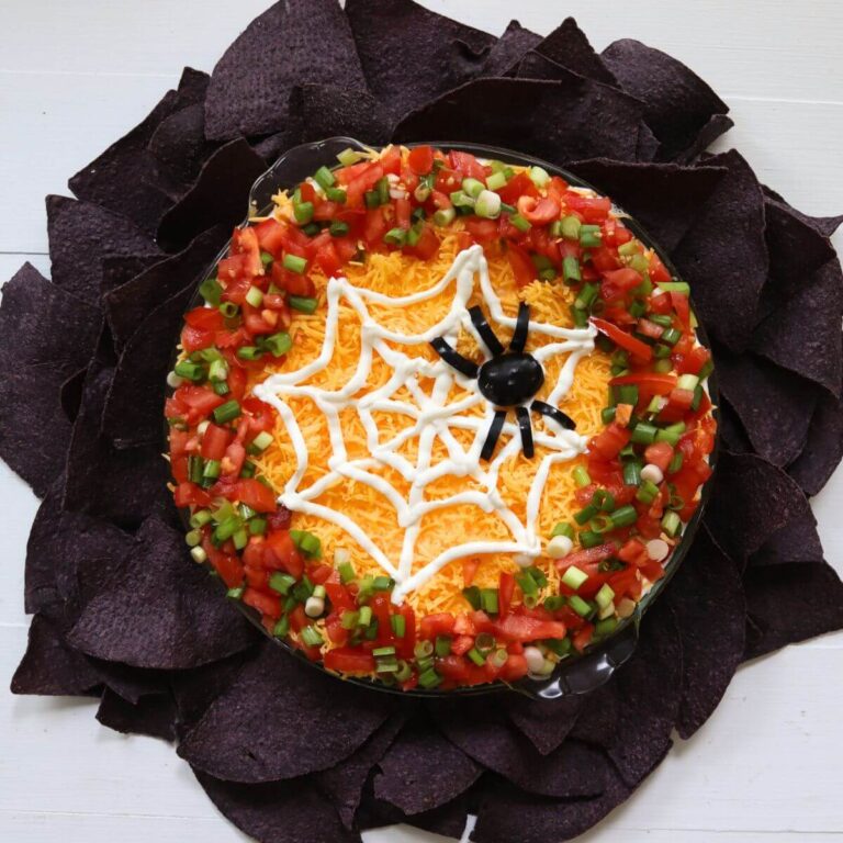 Spider web dip topped with a sour cream web, black olive spider, tomatoes, scallions, and cheddar cheese.