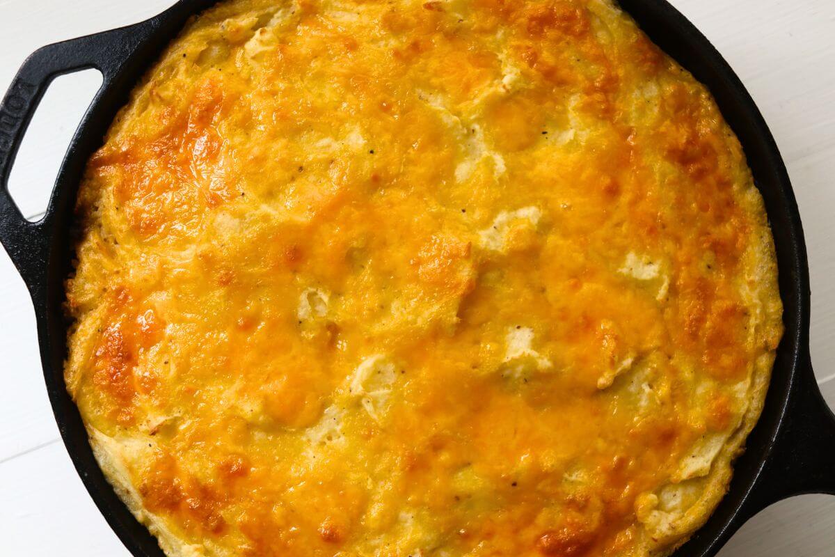 Golden baked cheddar and mashed potato topping on traditional cottage pie in a cast iron skillet.