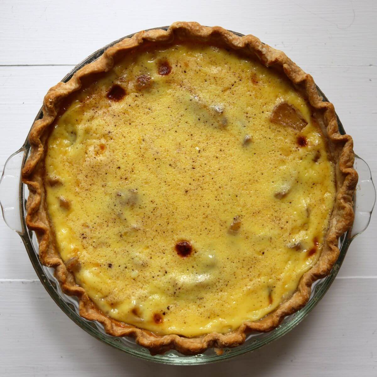 Apple custard pie with a golden crust, creamy custard filling, and visible pieces of apple.