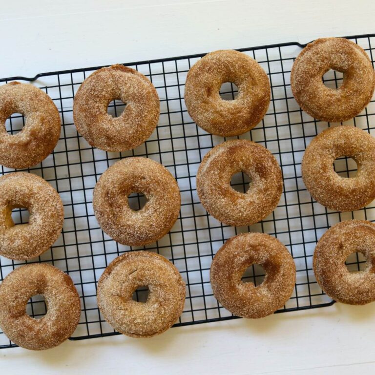 Baked apple cider donuts with cinnamon sugar coating cooling on a wire rack.