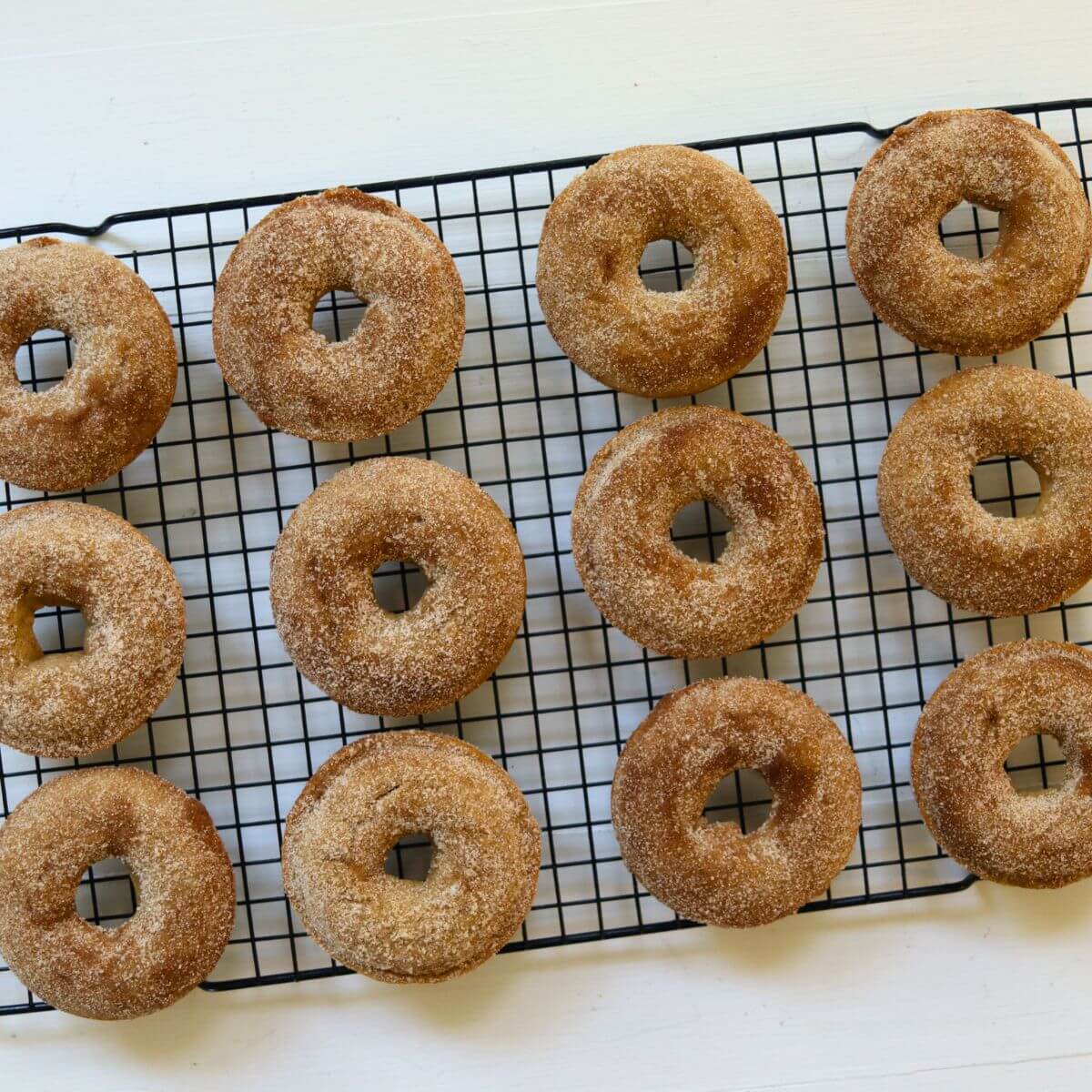 Baked apple cider donuts with cinnamon sugar coating cooling on a wire rack.