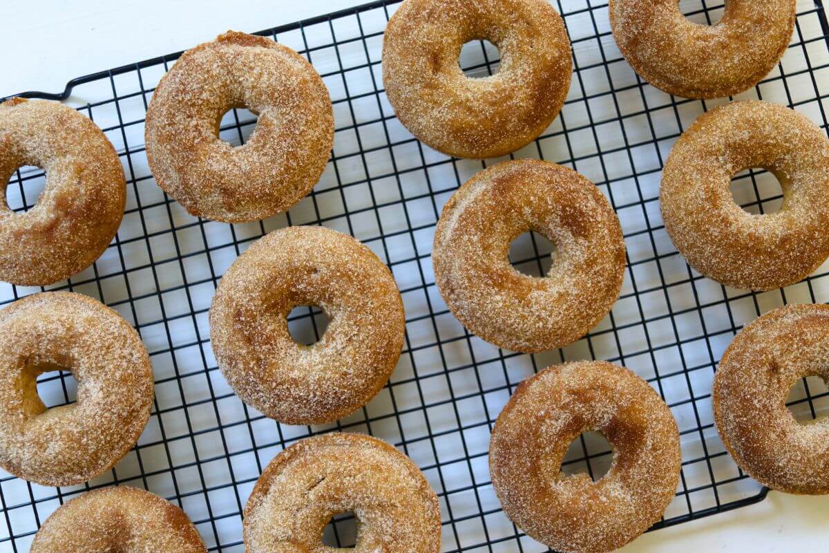 Cinnamon sugar coated baked apple cider donuts arranged on a black wire cooling rack.