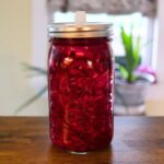 Shredded cabbage and beets fermenting in deep red brine inside a glass mason jar.