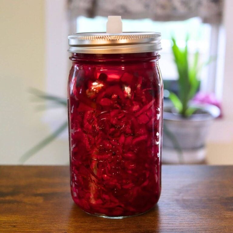 Shredded cabbage and beets fermenting in deep red brine inside a glass mason jar.