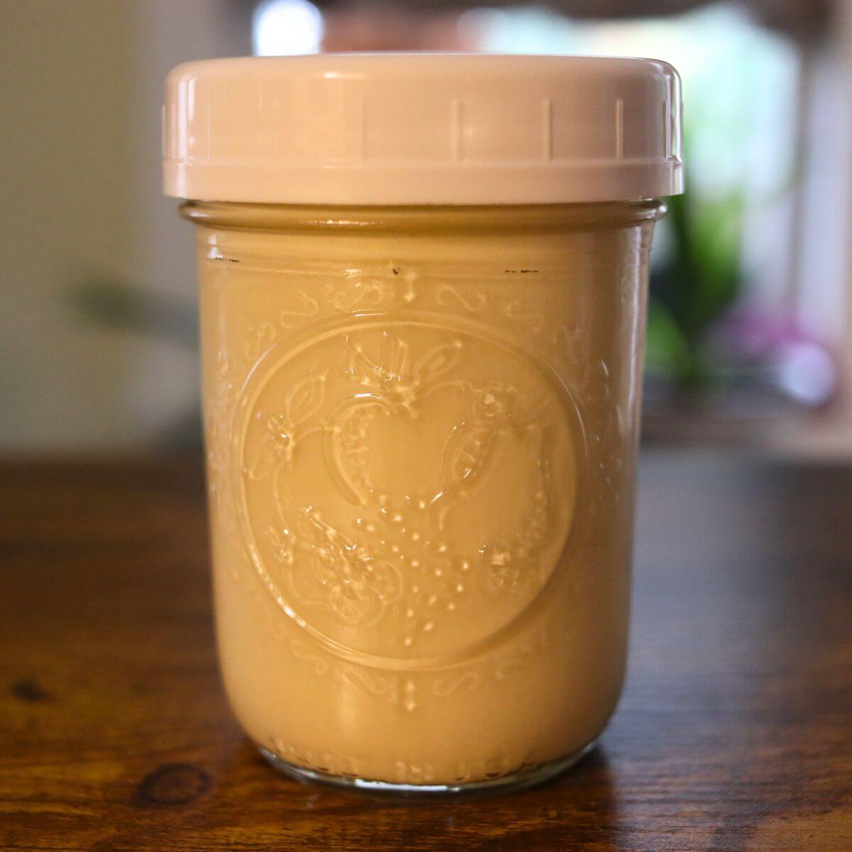 Homemade brown sugar creamer in a covered glass jar on a wooden table.