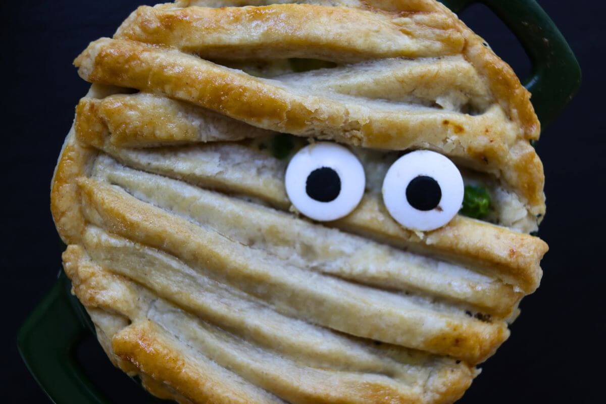 Mummy chicken pot pie with golden strips of pie crust and candy eyes peeking through.