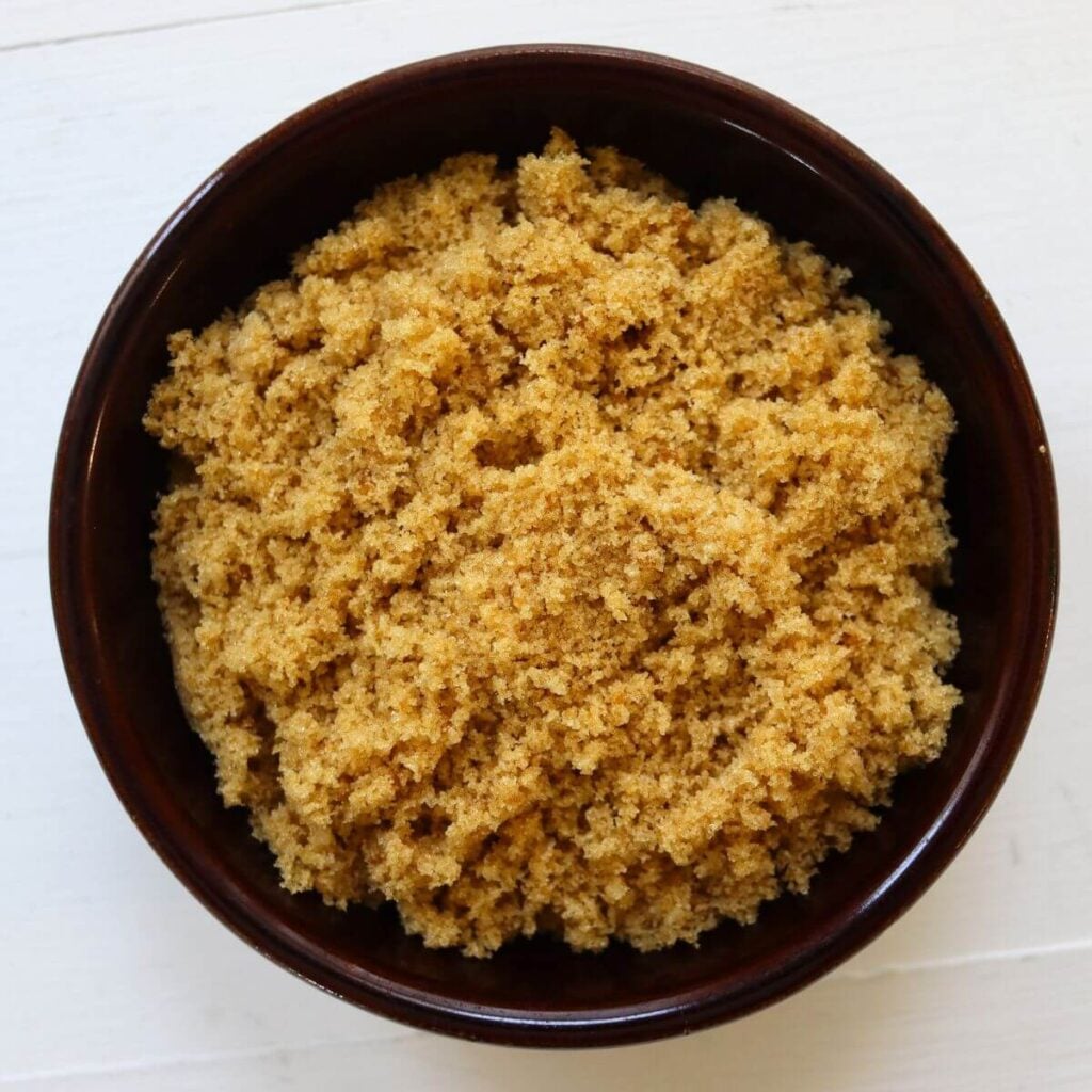 Homemade brown sugar with a soft, moist texture in a dark brown bowl.