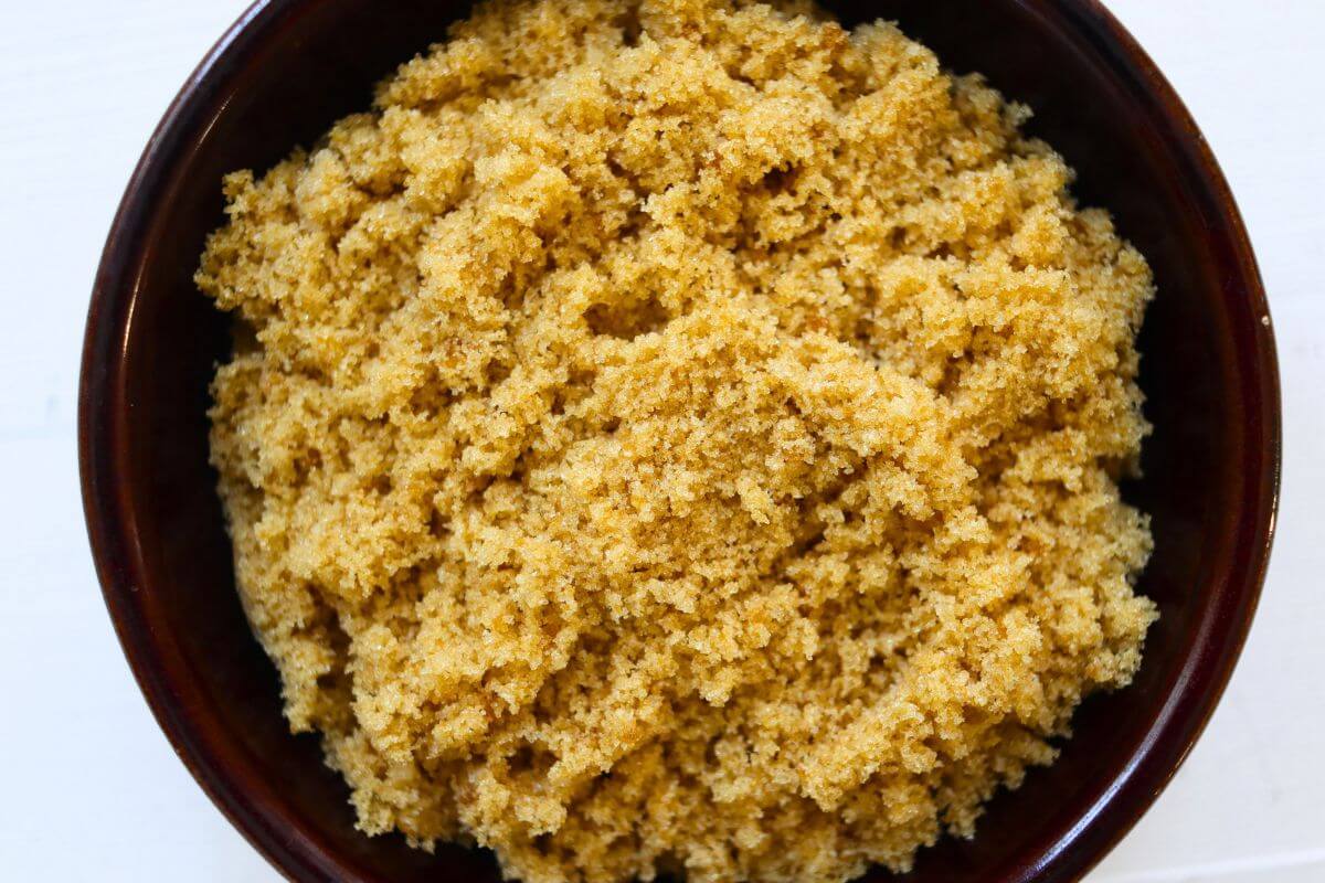 Soft homemade brown sugar piled in a dark brown bowl on a white surface.
