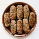 Homemade garlic basil sausage links with golden brown exteriors arranged on a brown ceramic serving plate.