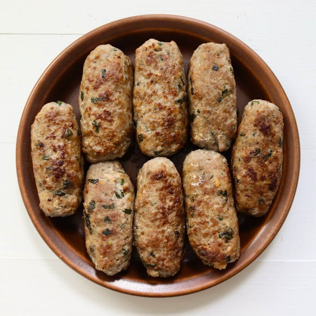 Homemade garlic basil sausage links with golden brown exteriors arranged on a brown ceramic serving plate.