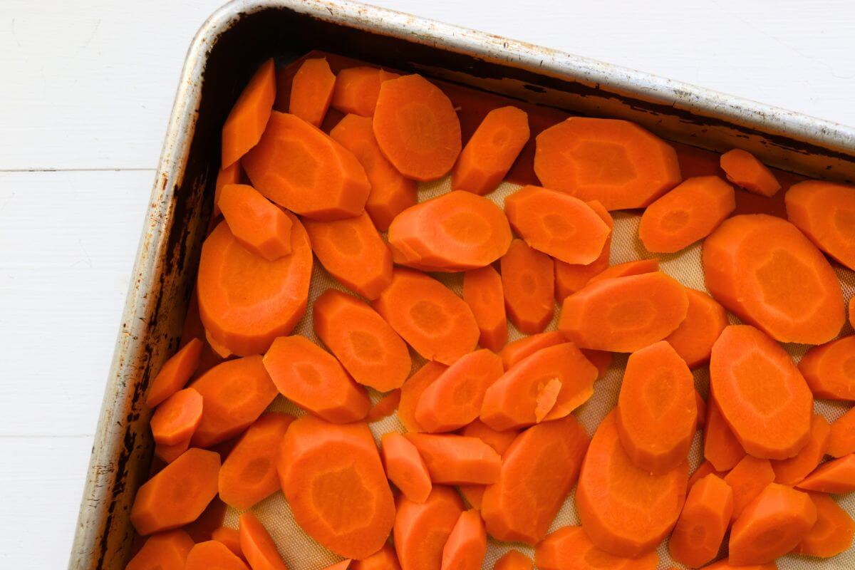 Diagonal carrot slices spread on a silicone-lined baking sheet for freezing.