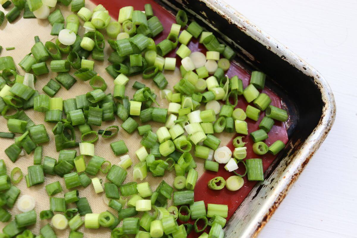 Sliced green onions spread on a silicone-lined baking sheet before freezing.