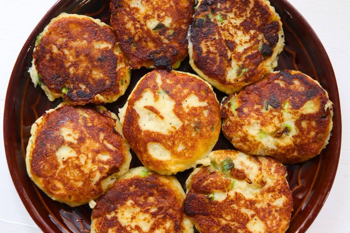 Golden brown mashed potato patties with scallions arranged on a brown serving plate.