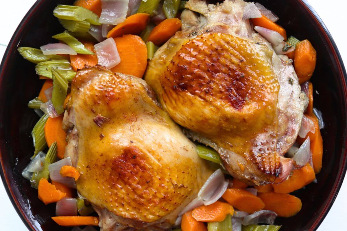 Two golden brown roasted turkey thighs with carrots, celery, and onions in a
serving bowl.