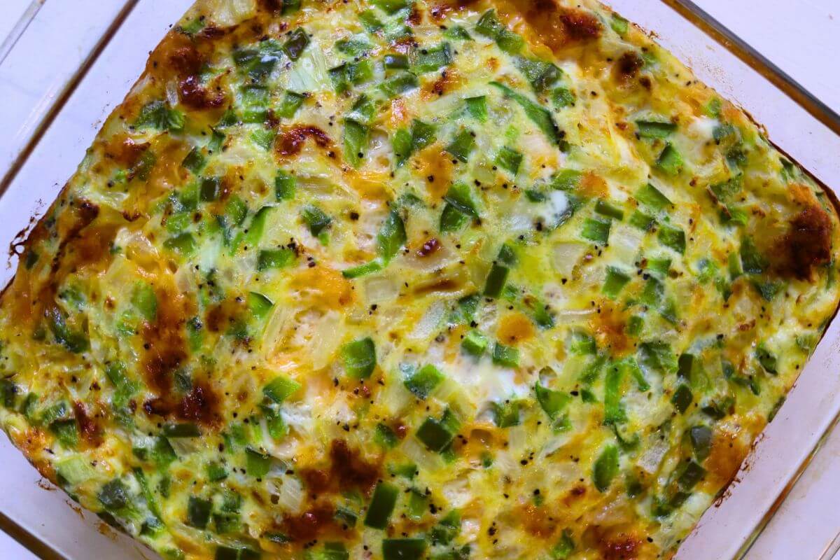 Baked Western egg casserole with green bell peppers, onions, and melted cheddar cheese in a glass baking dish.