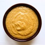 Homemade apple cider mustard with a thick, slightly coarse texture in a dark brown bowl.