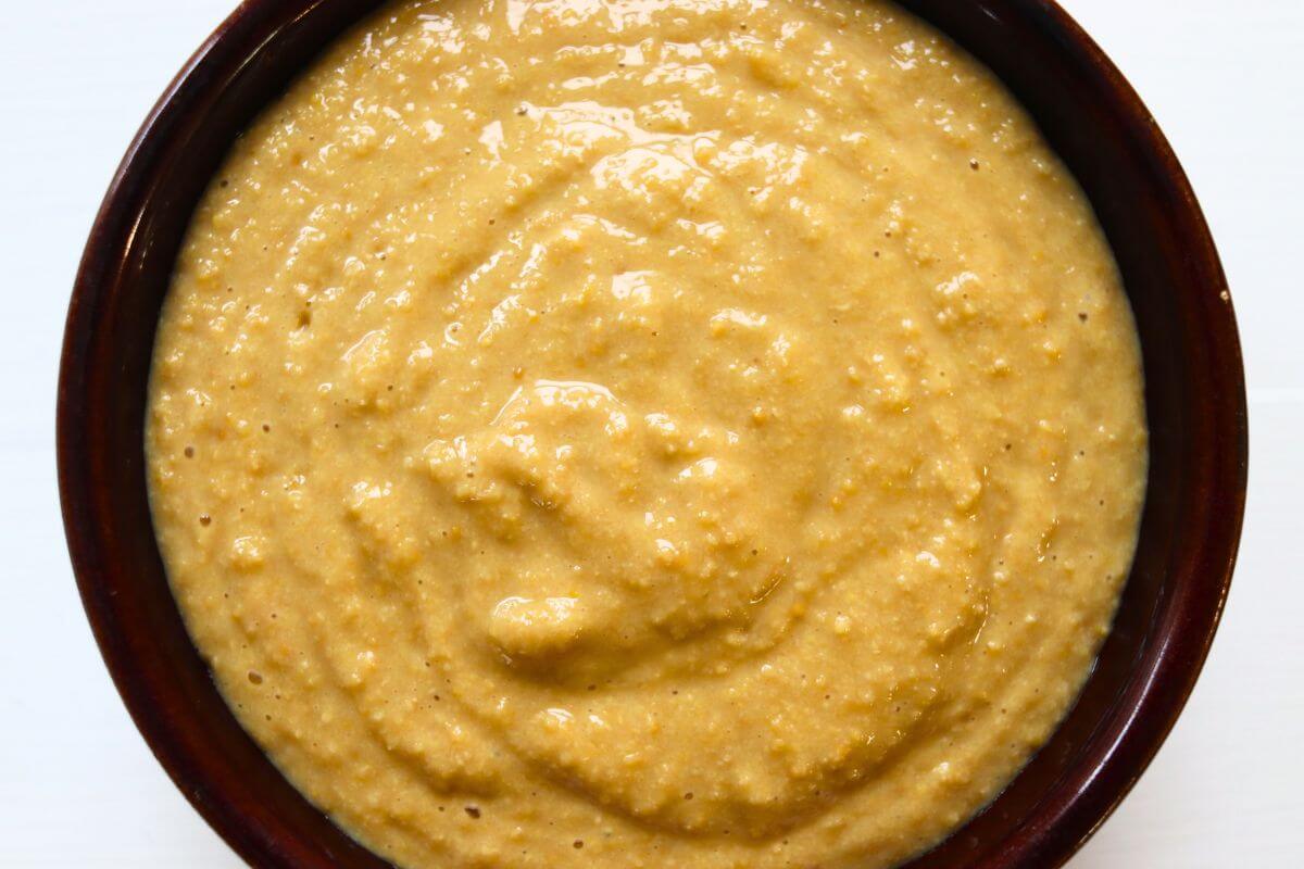 Golden yellow apple cider mustard with a creamy, grainy texture in a round brown bowl.