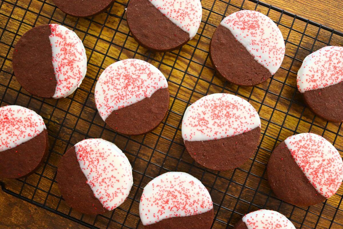 Chocolate sugar cookies with white chocolate coating and red sugar crystals arranged on a black wire rack.