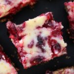 Cranberry cheesecake bars arranged on a dark surface, showing marbled cranberry topping and graham cracker crust.