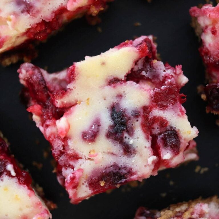Cranberry cheesecake bars arranged on a dark surface, showing marbled cranberry topping and graham cracker crust.