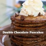 Double chocolate pancakes topped with whipped cream and chocolate chips, with text reading “Double Chocolate Pancakes".