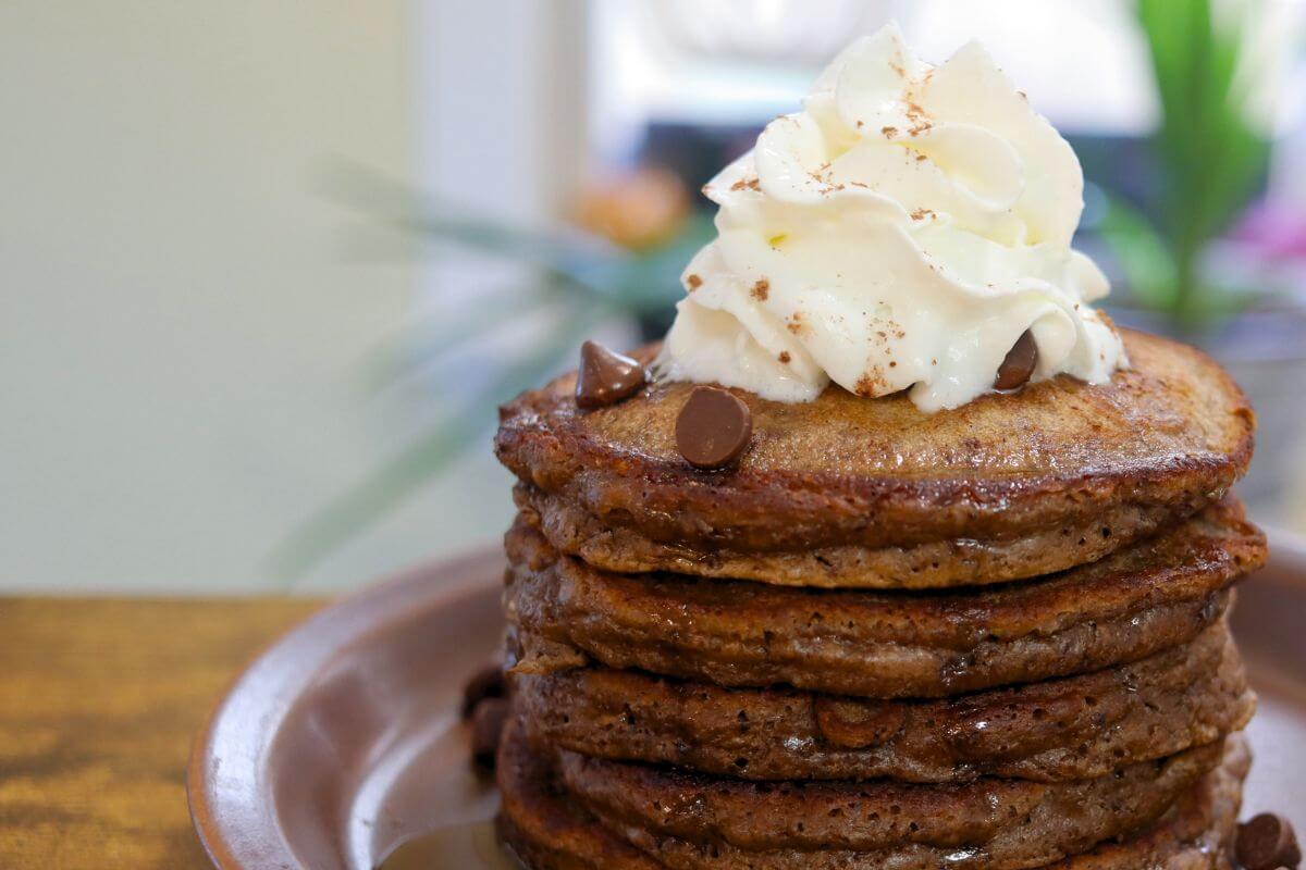 Double chocolate pancakes with golden-brown edges, chocolate chips, and a generous swirl of whipped cream.