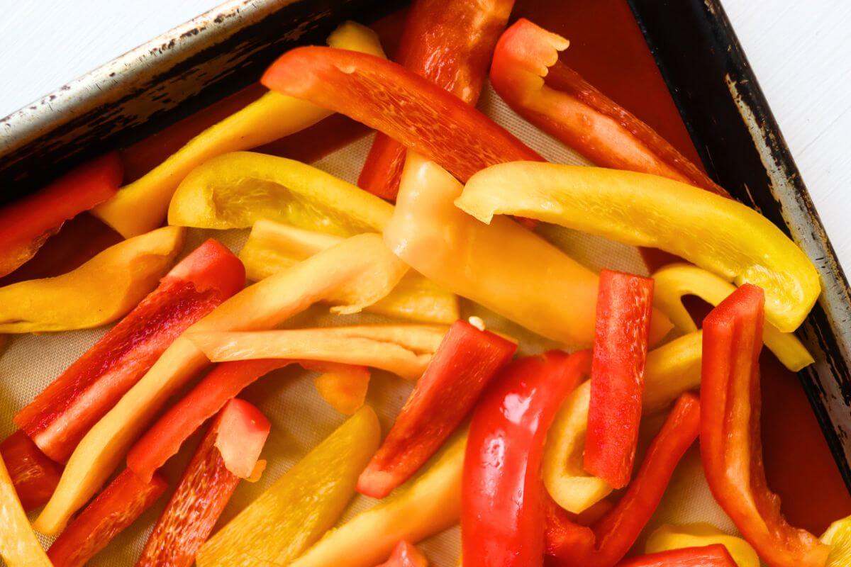 Sliced red, yellow, and orange bell peppers arranged on a parchment-lined baking sheet for freezing.